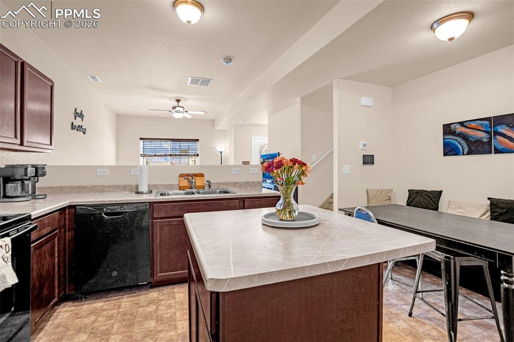 Kitchen with light countertops, black appliances, dark wood finish cabinetry, a kitchen island, and a peninsula