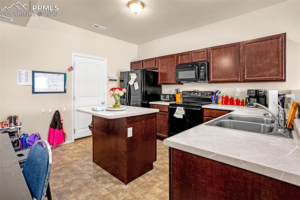 Kitchen featuring black appliances, light countertops, a kitchen island, and light floors