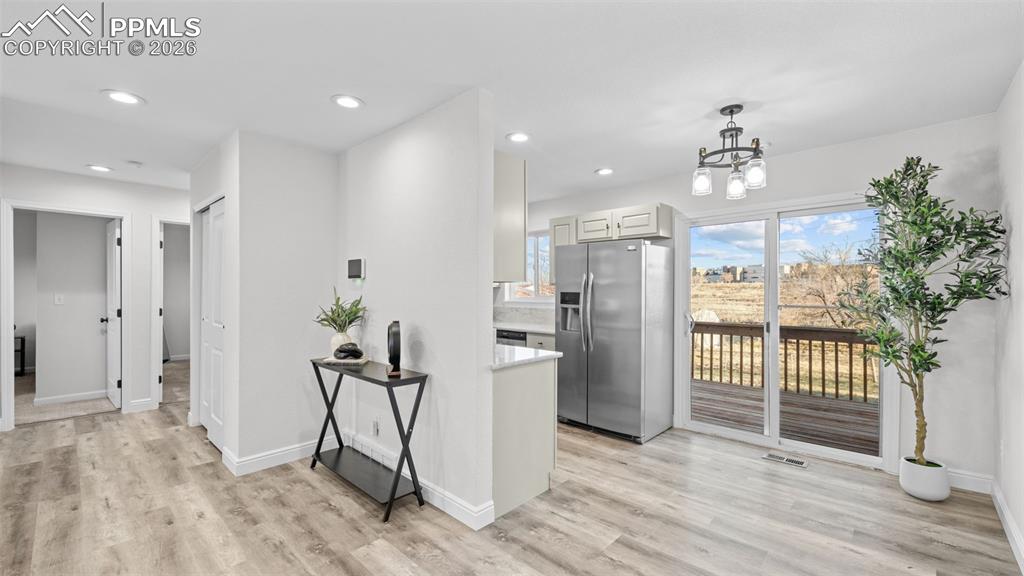 Kitchen with stainless steel fridge with ice dispenser, hanging lights, light wood-style flooring, light stone counters, and white cabinets