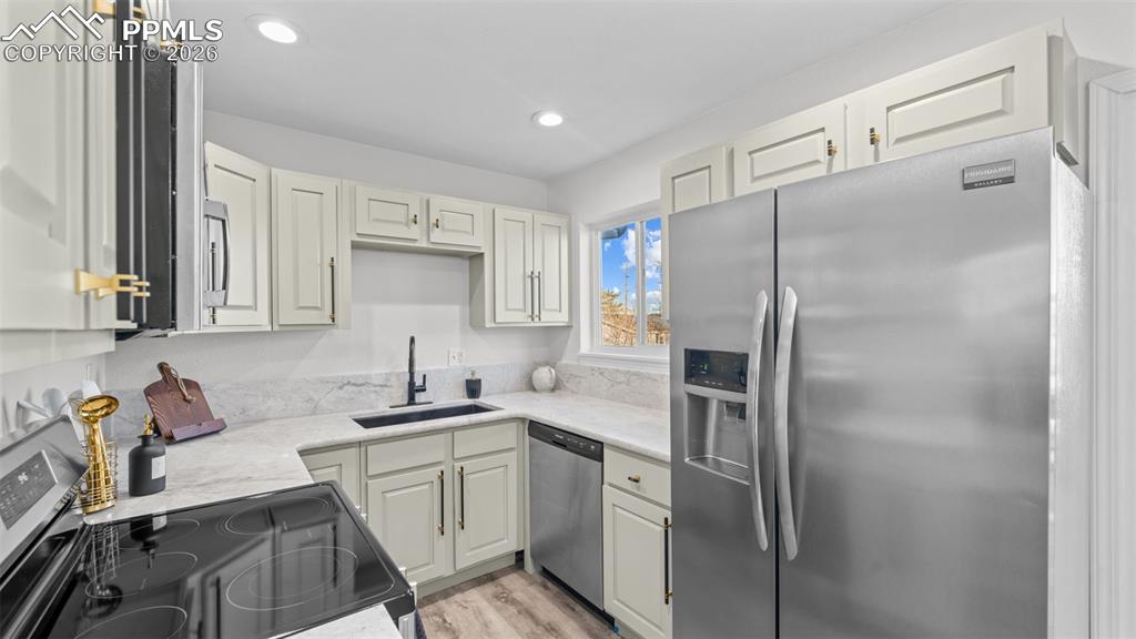 Kitchen with stainless steel appliances, light stone counters, recessed lighting, light wood finished floors, and white cabinetry