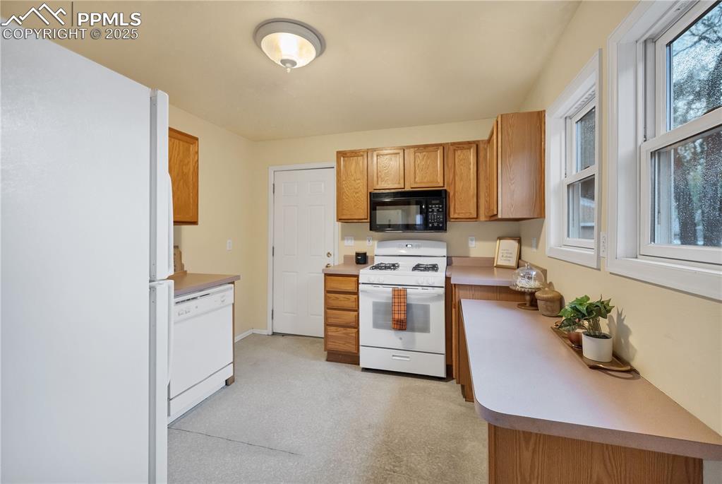 Kitchen with white appliances, light countertops, brown cabinets, and light colored carpet