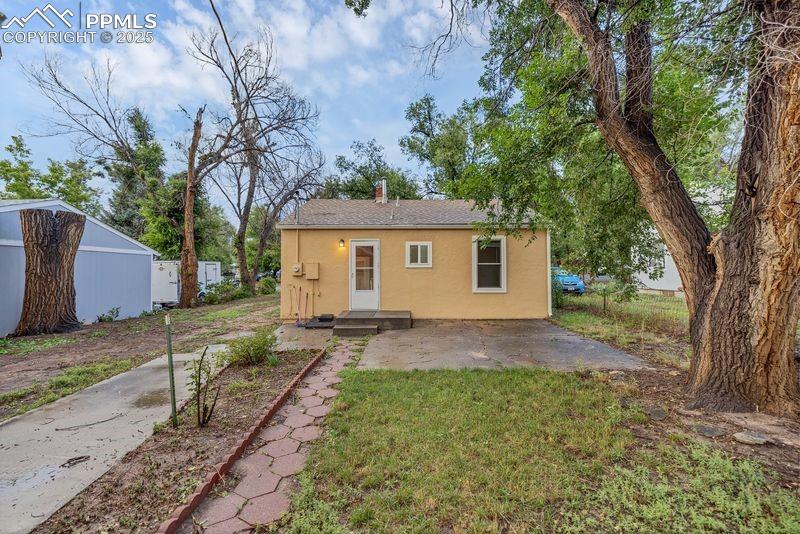 Back of house with stucco siding, a yard, a chimney, a shingled roof, and a patio