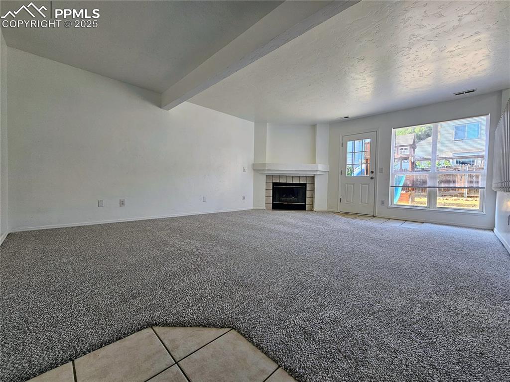 Unfurnished living room with light tile patterned floors, beamed ceiling, a tiled fireplace, light colored carpet, and a textured ceiling