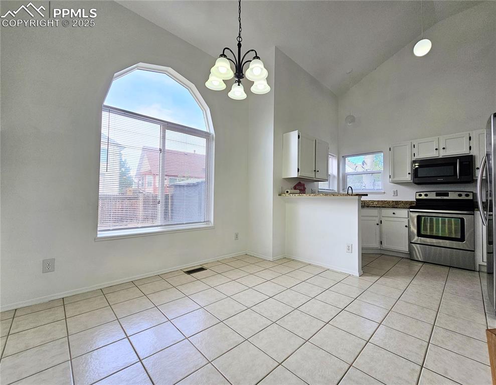 Kitchen featuring appliances with stainless steel finishes, white cabinetry, light tile patterned floors, hanging light fixtures, and a peninsula