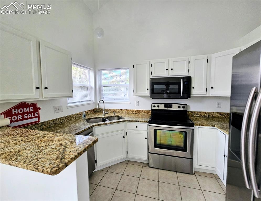 Kitchen featuring appliances with stainless steel finishes, white cabinets, dark stone countertops, light tile patterned flooring, and a peninsula