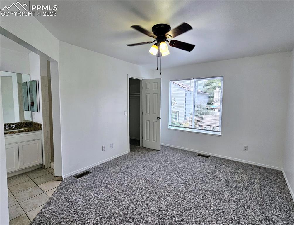 Unfurnished bedroom featuring light carpet, a closet, a ceiling fan, light tile patterned floors, and connected bathroom
