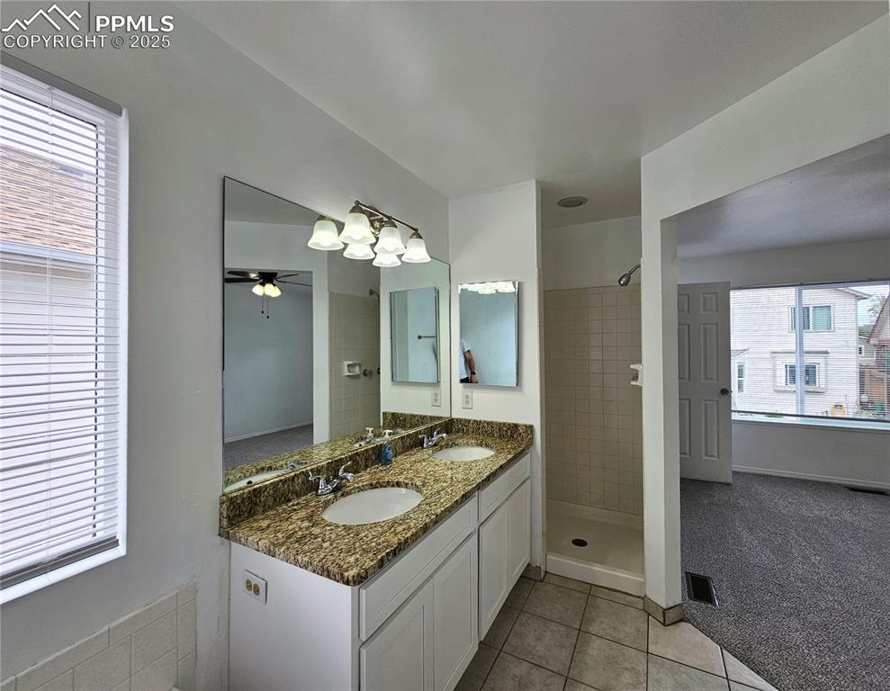 Bathroom with double vanity, light tile patterned floors, a shower stall, and a ceiling fan