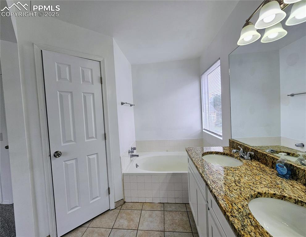 Full bathroom featuring a bath, light tile patterned floors, double vanity, and a chandelier