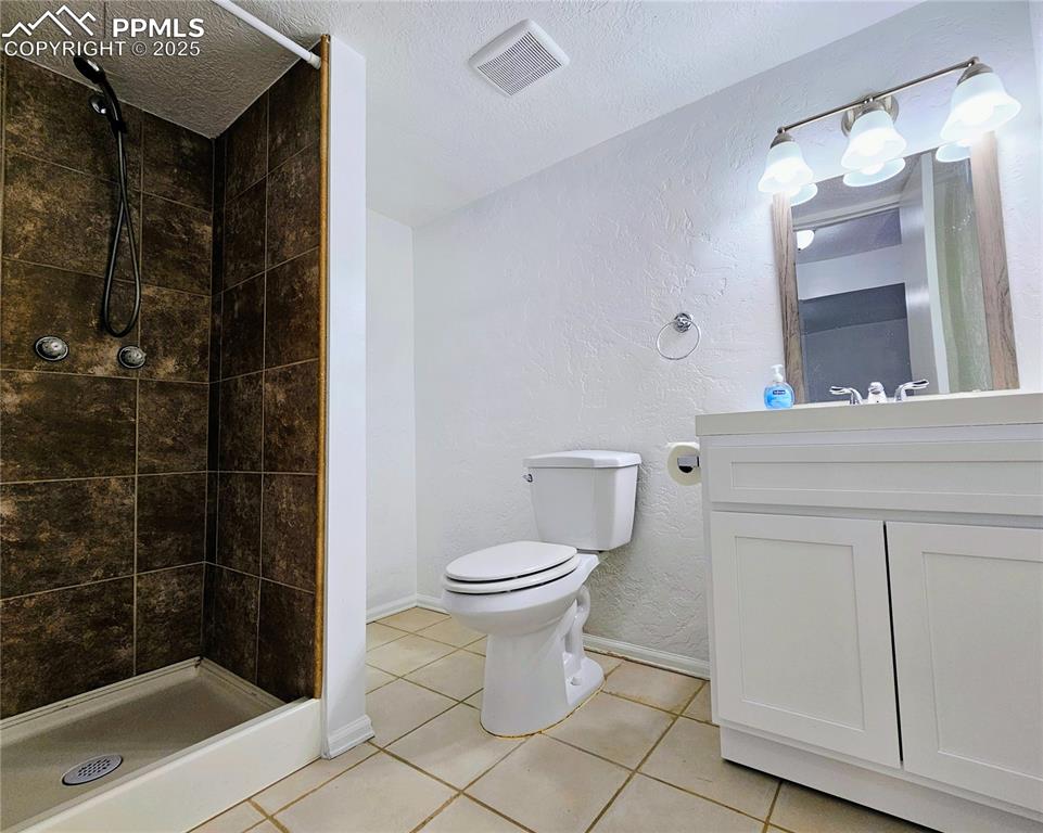 Full bath with a textured wall, light tile patterned floors, vanity, a shower stall, and a textured ceiling