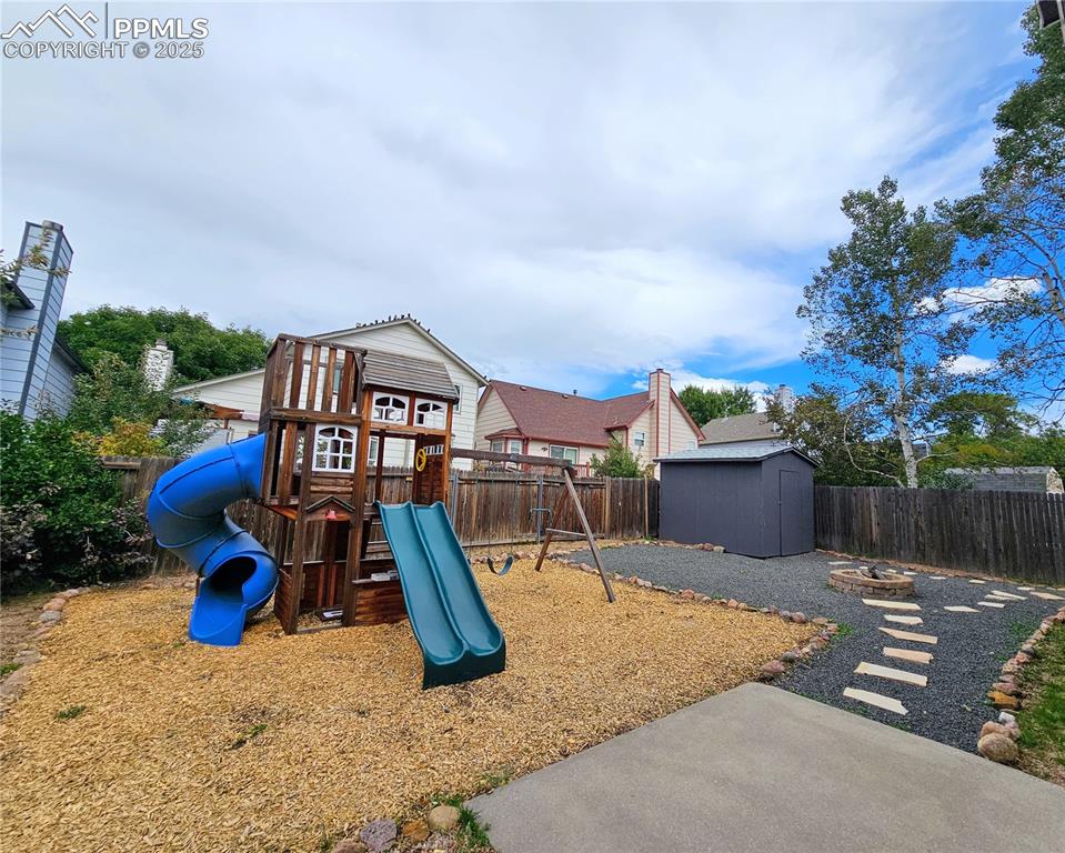View of jungle gym featuring a fenced backyard, a fire pit, and a storage shed