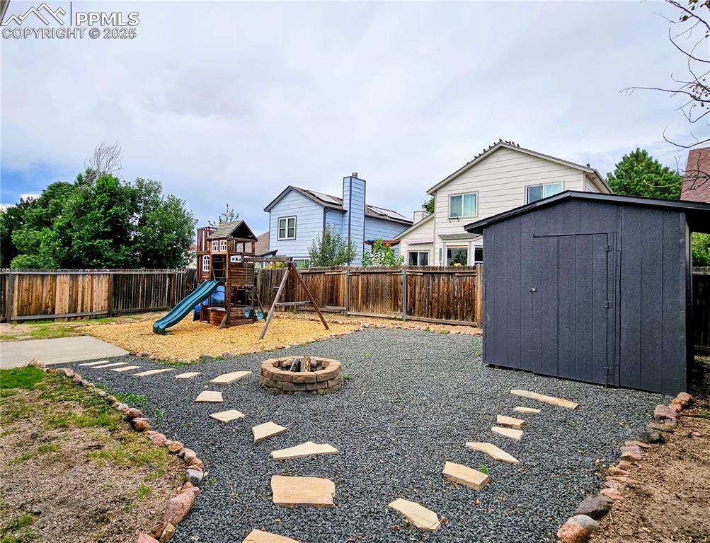 Fenced backyard with a fire pit, a shed, and a playground