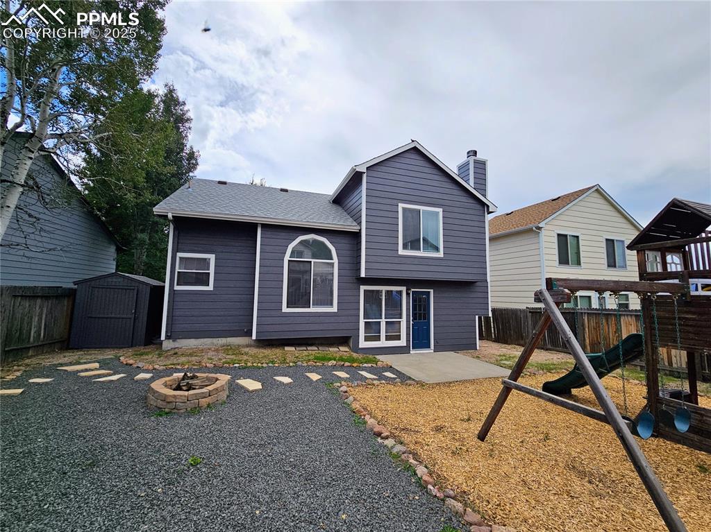 Rear view of house with a playground, a fenced backyard, a fire pit, a storage unit, and a chimney
