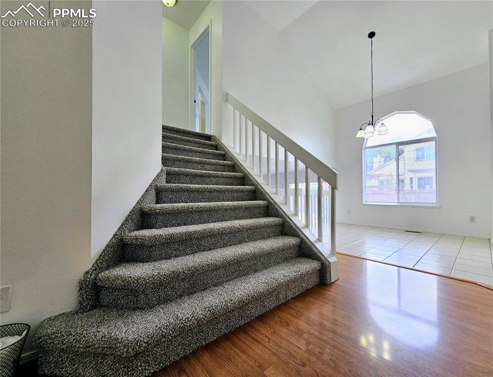 Stairway featuring wood finished floors, a chandelier, and high vaulted ceiling