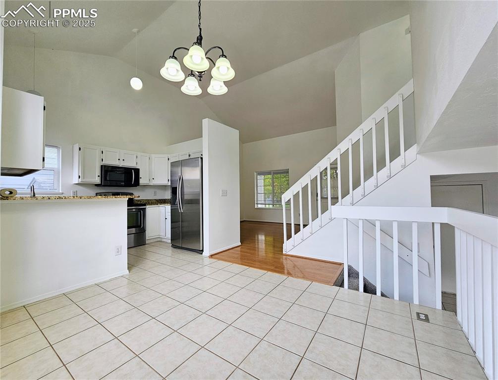 Kitchen featuring white cabinetry, stainless steel appliances, a chandelier, hanging light fixtures, and high vaulted ceiling