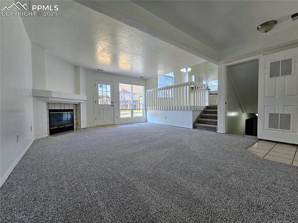 Unfurnished living room featuring light carpet, stairs, a textured ceiling, and a tile fireplace