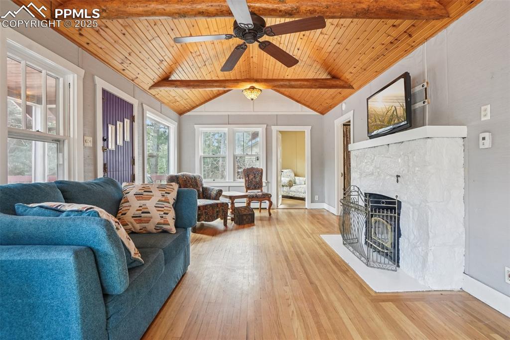 Living room with wood flooring, wood ceilings accentuated by wood beams, a wood burning stove and walk out to main deck