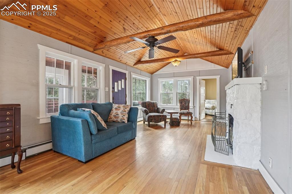 Living room with wood flooring, wood ceilings accentuated by wood beams, a wood burning stove and walk out to main deck