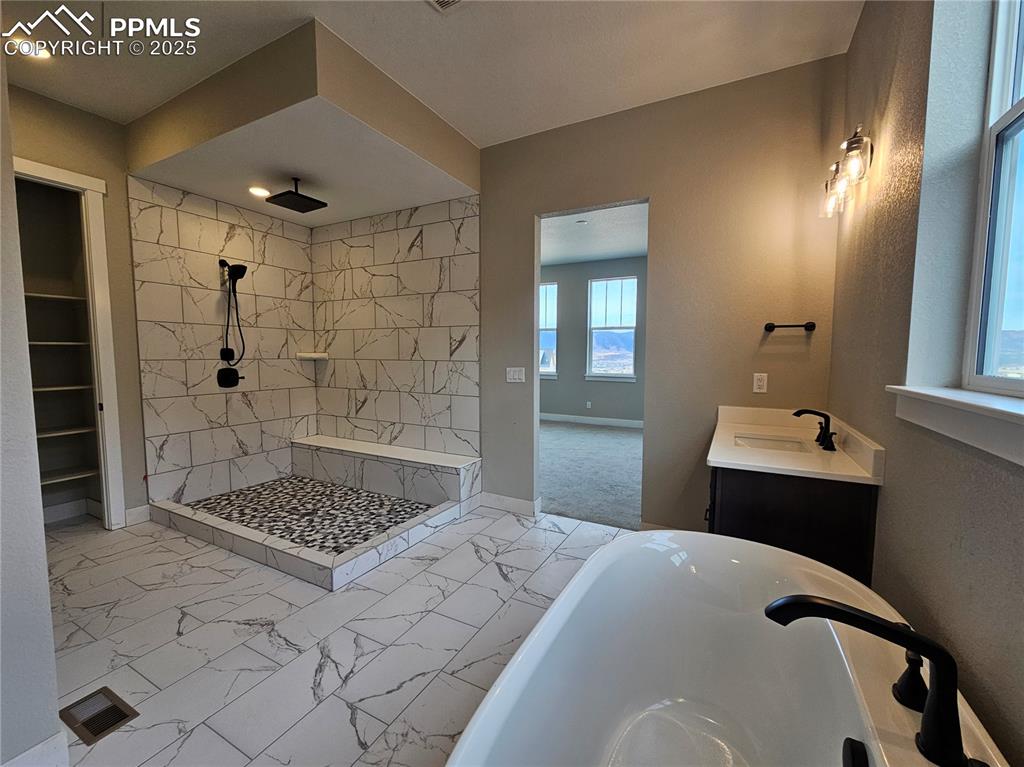 Full bath with a freestanding tub, vanity, light marble finish flooring, tiled shower, and a walk in closet