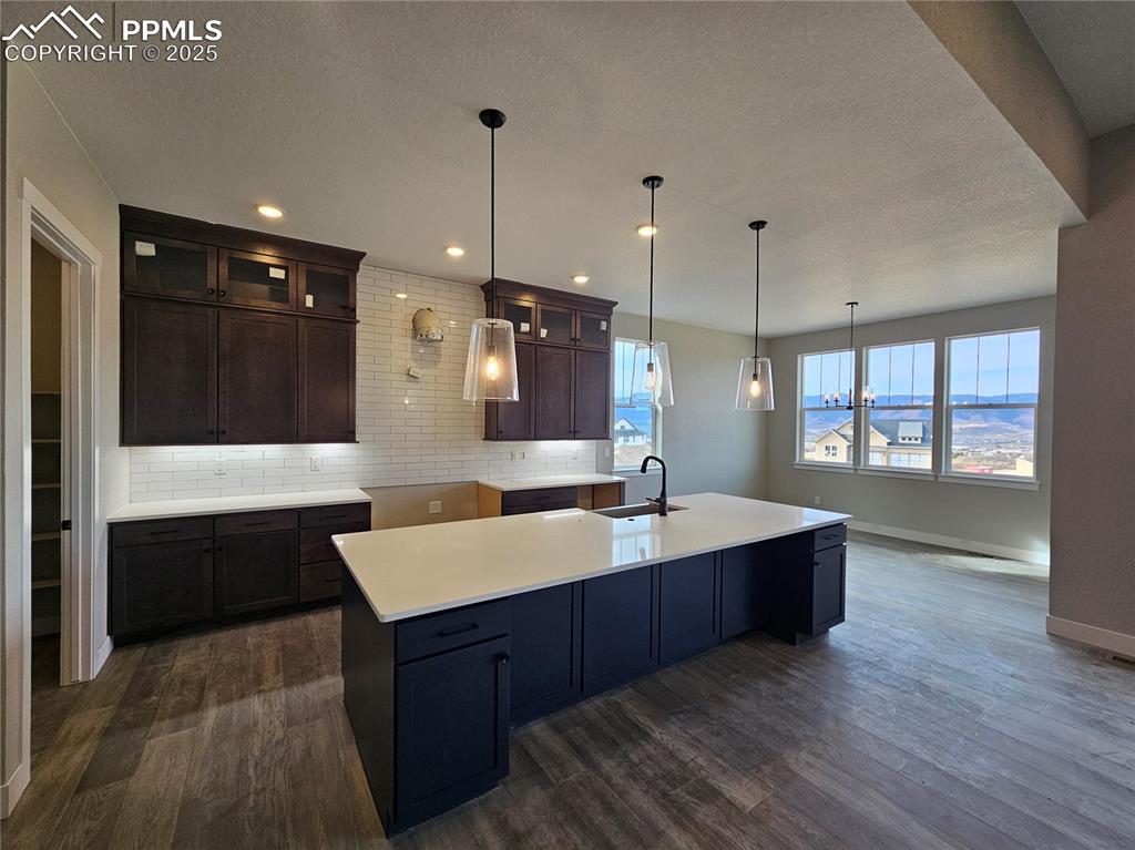 Kitchen with dark brown cabinets, backsplash, glass insert cabinets, pendant lighting, and a textured ceiling