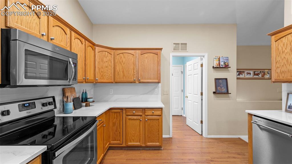 Kitchen with appliances with stainless steel finishes, light wood-style floors, light stone countertops, and brown cabinetry