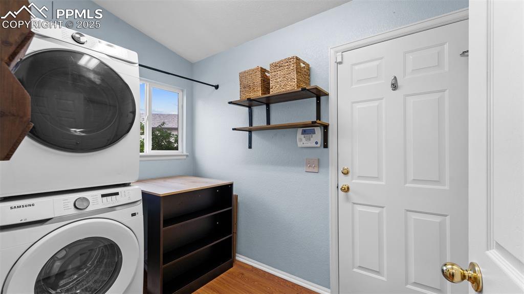 Laundry room with light wood-style flooring, stacked washer and clothes dryer, and a textured wall