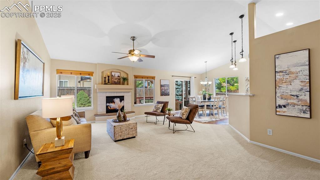 Living area with ceiling fan, plenty of natural light, a tiled fireplace, carpet, and high vaulted ceiling