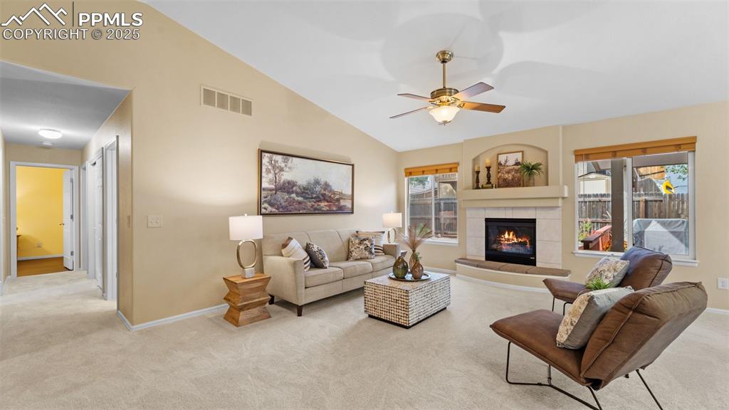 Living area with vaulted ceiling, light colored carpet, ceiling fan, plenty of natural light, and a tile fireplace