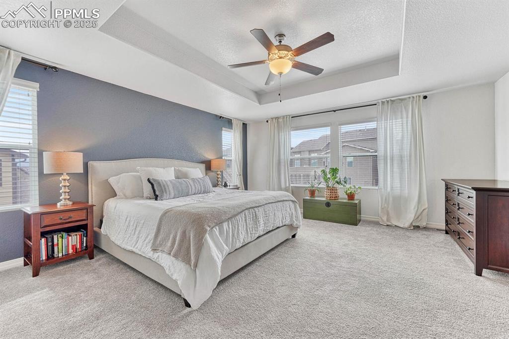 Bedroom with baseboards, light colored carpet, a tray ceiling, a textured ceiling, and a ceiling fan