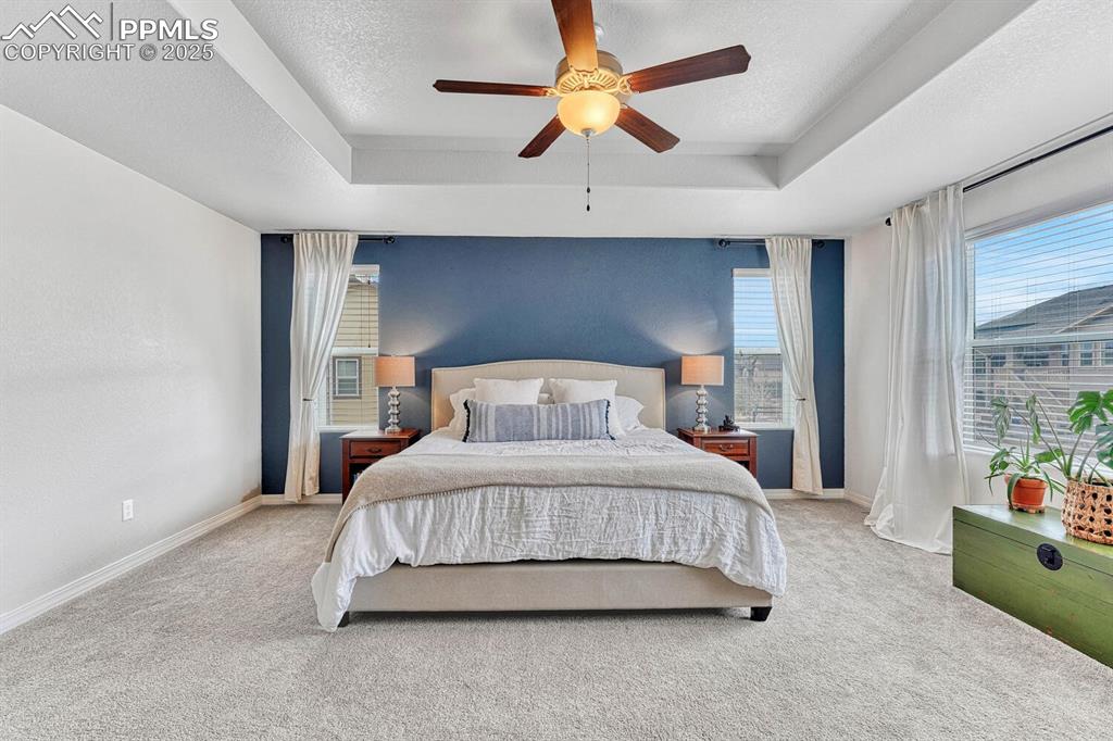 Carpeted bedroom featuring a tray ceiling, baseboards, a textured ceiling, and a ceiling fan