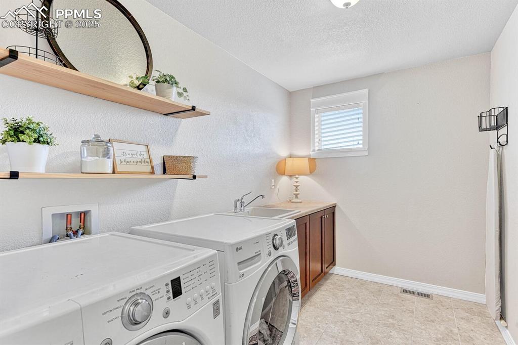 Clothes washing area with baseboards, visible vents, cabinet space, a sink, and washer and dryer