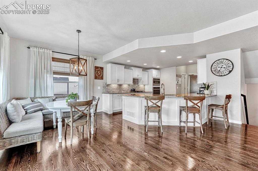 Kitchen featuring tasteful backsplash, dark wood-style floors, a peninsula, a breakfast bar area, and white cabinets