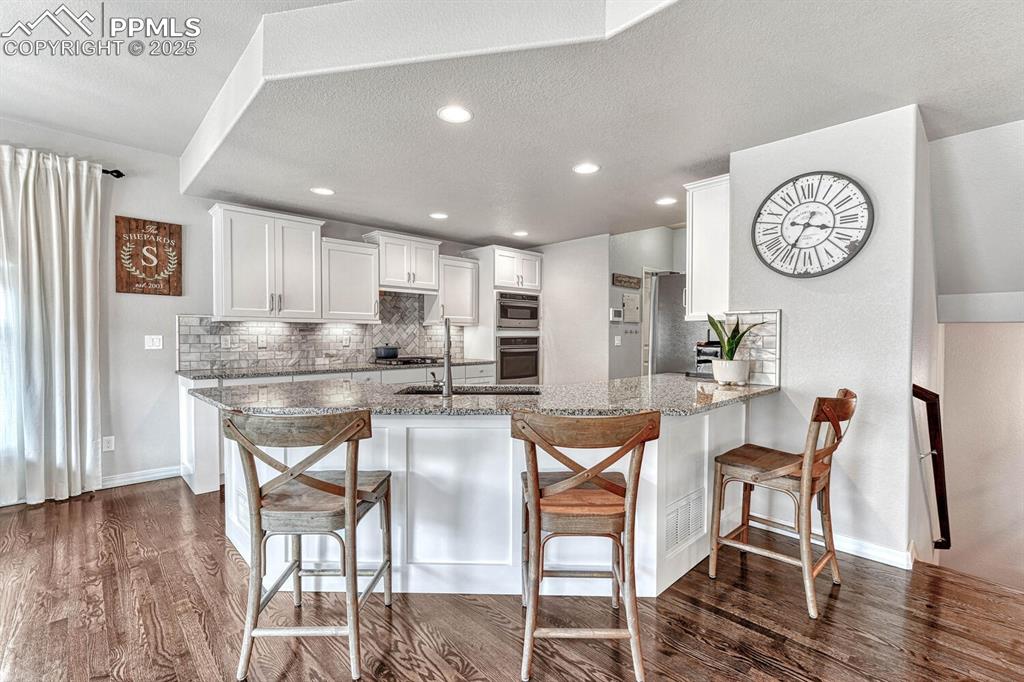 Kitchen with light stone countertops, dark wood finished floors, a breakfast bar, decorative backsplash, and white cabinetry