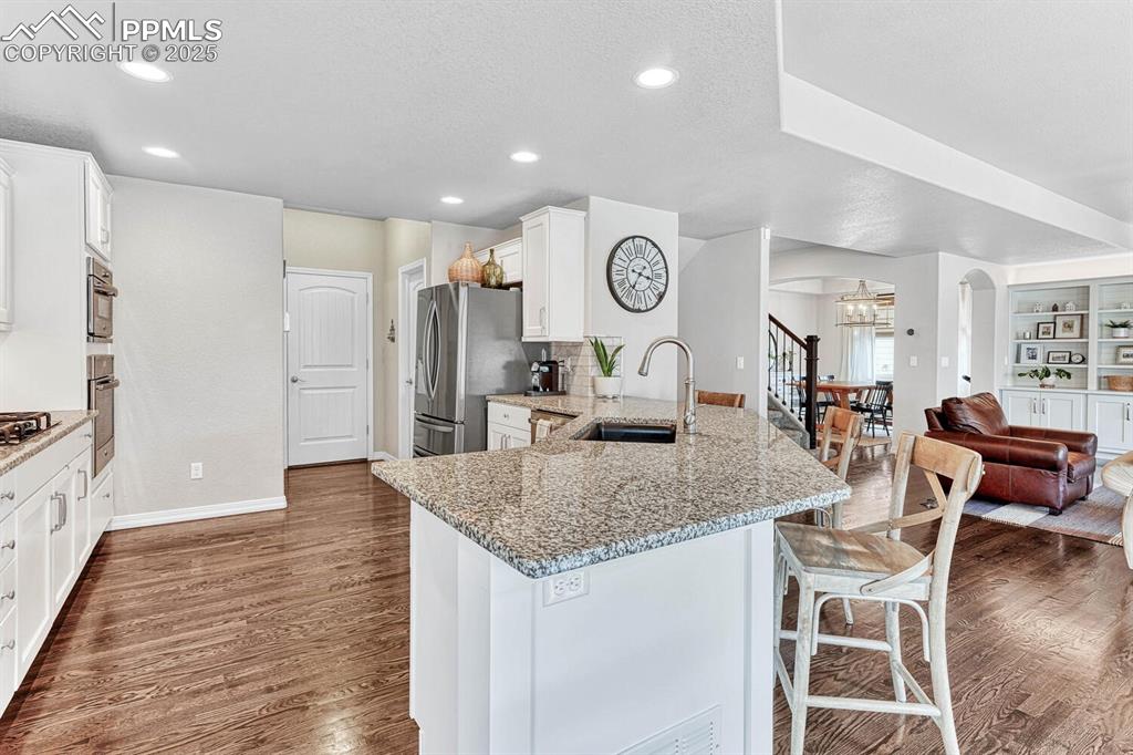 Kitchen with a sink, a peninsula, stainless steel refrigerator with ice dispenser, arched walkways, and dark wood-style flooring