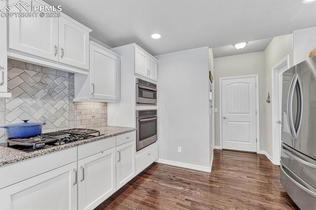 Kitchen featuring dark wood-style floors, stainless steel fridge, white cabinets, and black gas cooktop