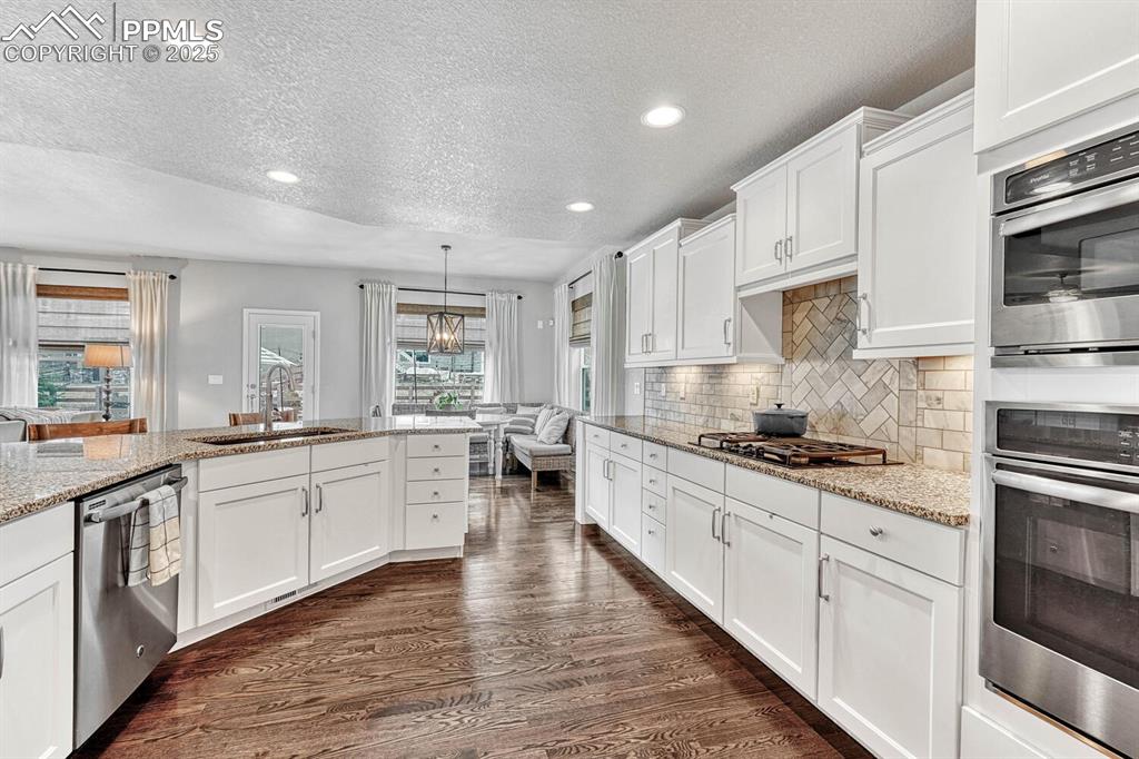 Kitchen featuring dark wood-style flooring, a sink, appliances with stainless steel finishes, white cabinetry, and backsplash