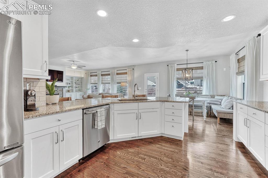 Kitchen with dark wood-style flooring, a sink, decorative backsplash, appliances with stainless steel finishes, and open floor plan