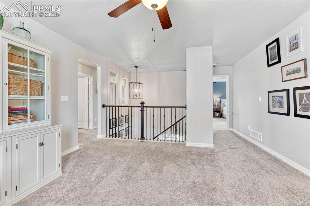 Carpeted empty room with ceiling fan with notable chandelier, baseboards, and visible vents