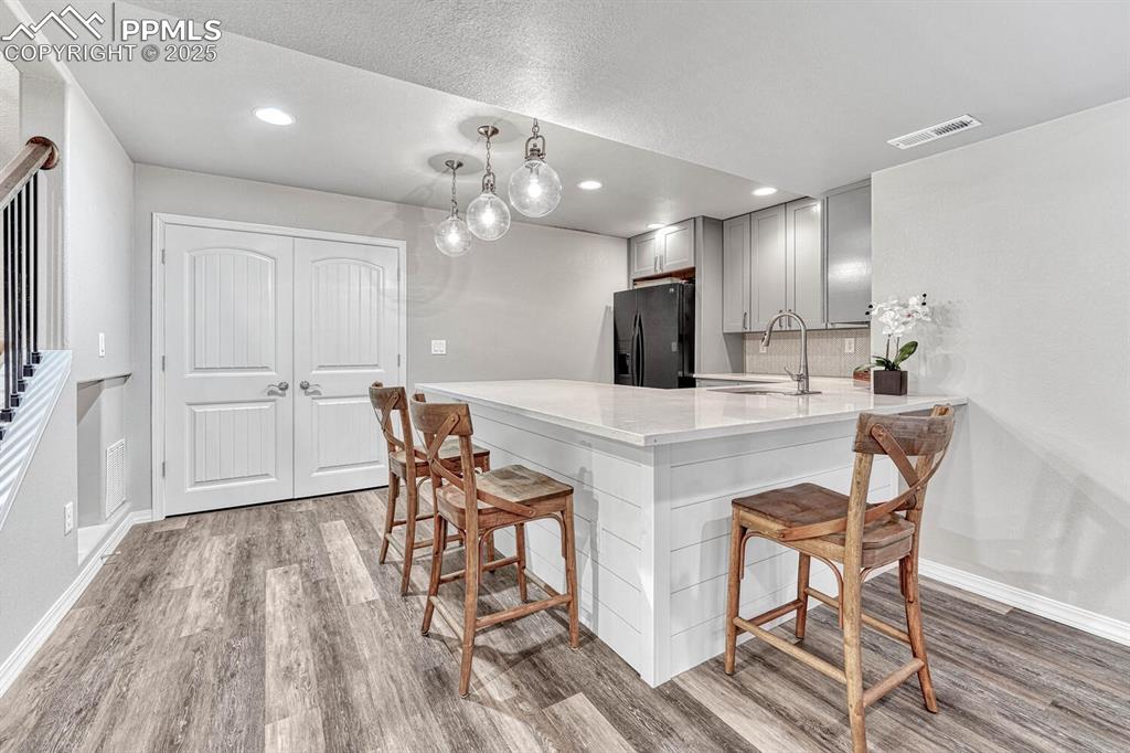 Kitchen featuring a breakfast bar area, visible vents, gray cabinets, a sink, and black fridge with ice dispenser