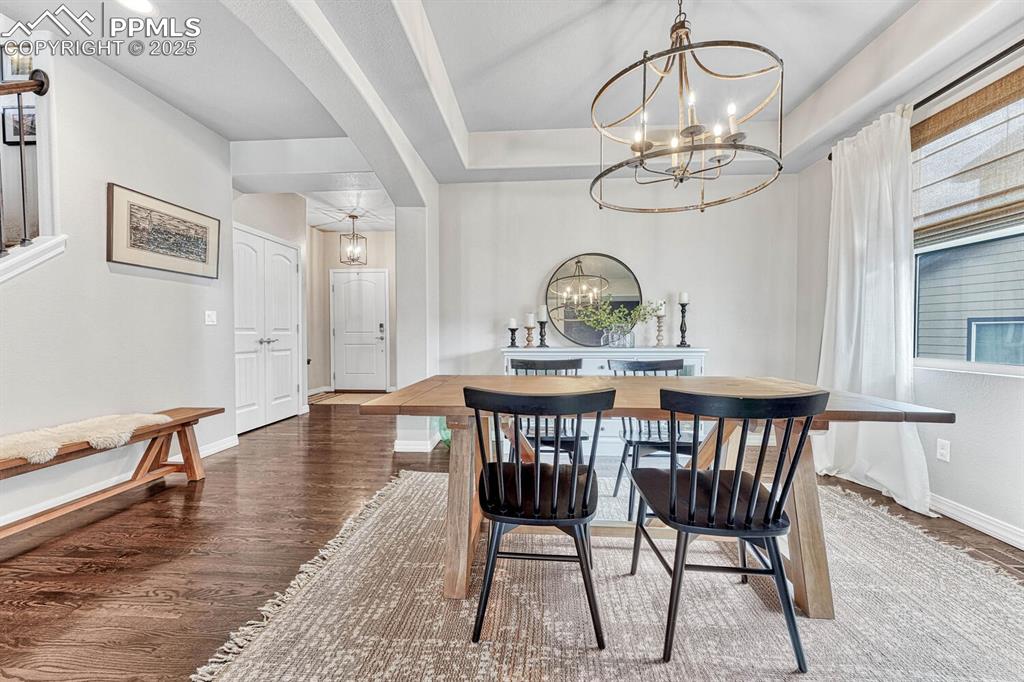 Dining room with wood finished floors, baseboards, an inviting chandelier, arched walkways, and a raised ceiling