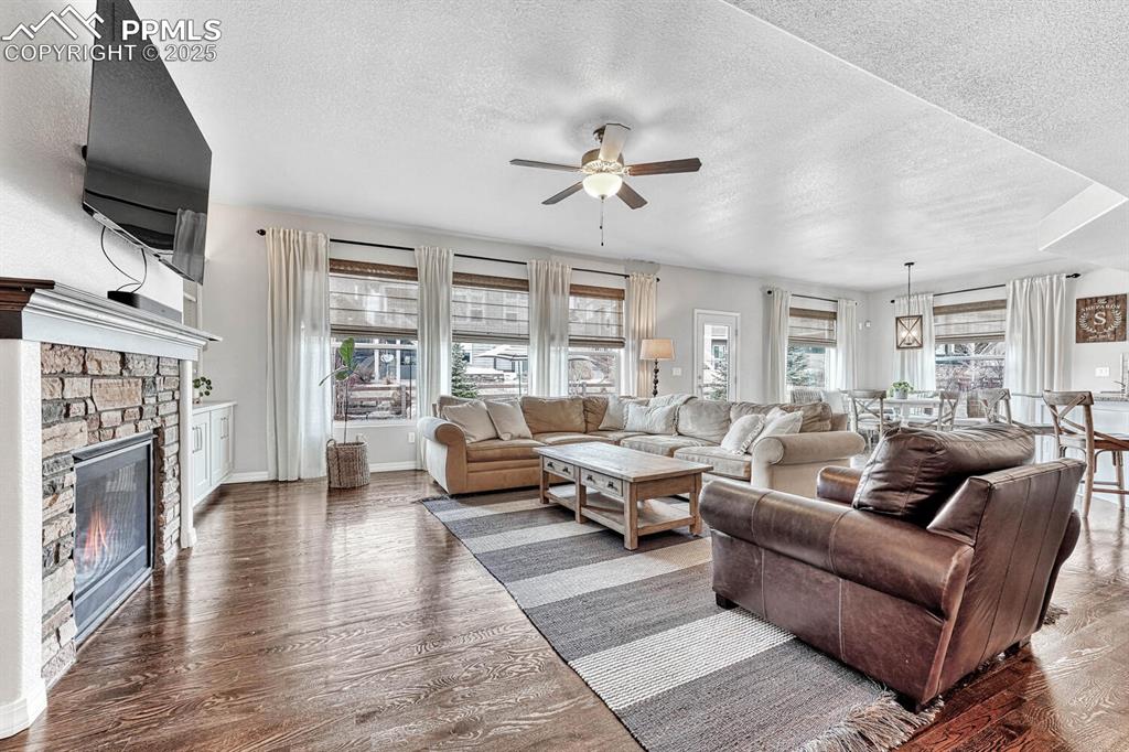 Living area with ceiling fan, a textured ceiling, wood finished floors, and a fireplace