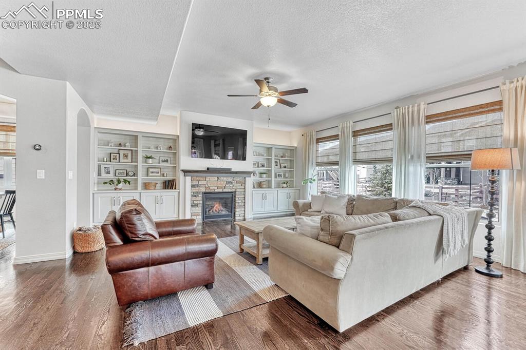 Living room featuring a stone fireplace, wood finished floors, and a textured ceiling