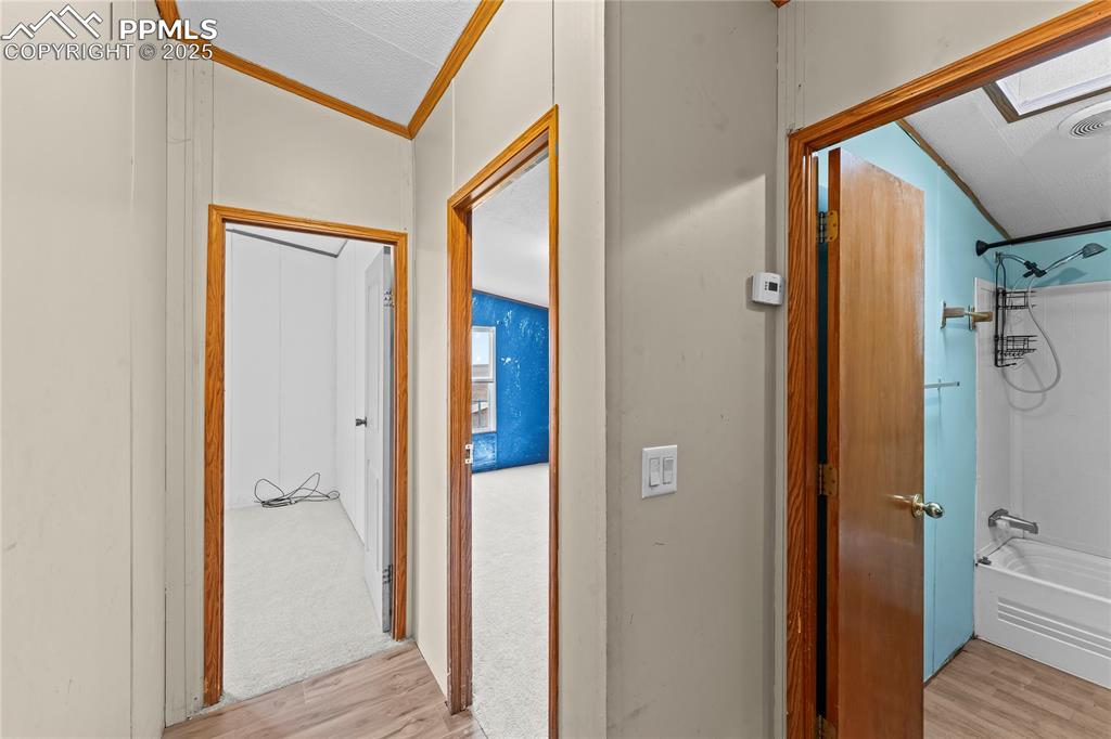 Hallway with a skylight, light wood-type flooring, ornamental molding, and vaulted ceiling