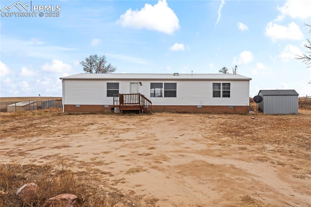 Back of house featuring crawl space, a shed, and a metal roof