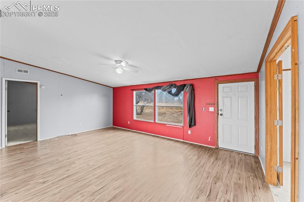 Unfurnished living room with crown molding, light wood-style flooring, ceiling fan, and lofted ceiling
