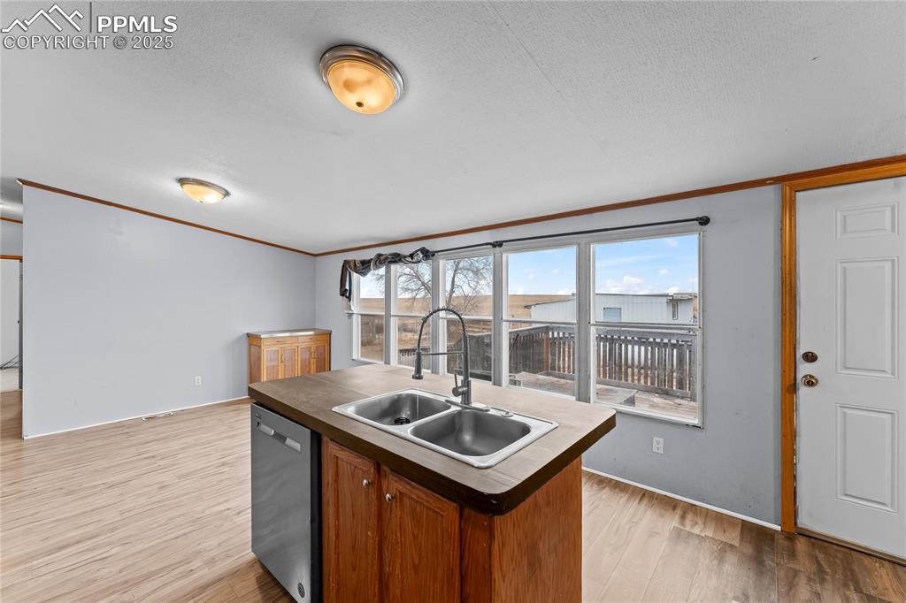 Kitchen featuring a kitchen island with sink, stainless steel dishwasher, light wood-type flooring, brown cabinets, and ornamental molding