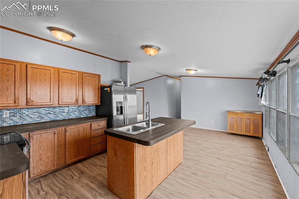 Kitchen featuring a kitchen island with sink, backsplash, dark countertops, brown cabinets, and ornamental molding
