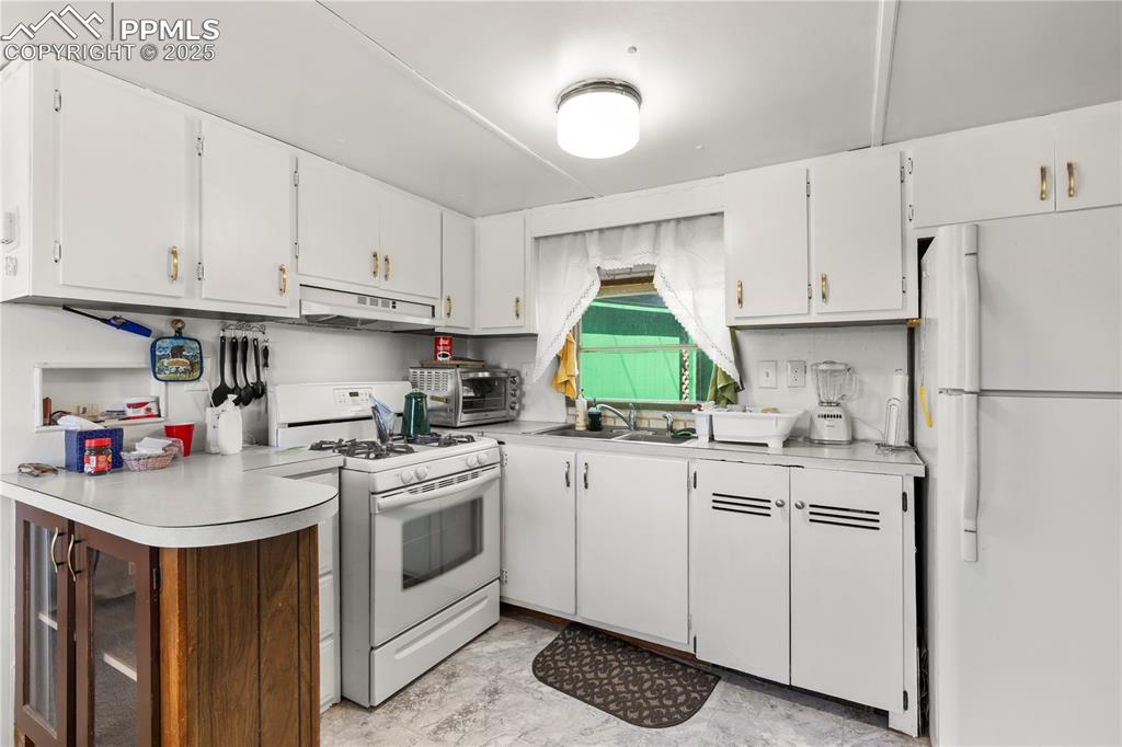 Kitchen with white appliances, white cabinetry, light countertops, and under cabinet range hood