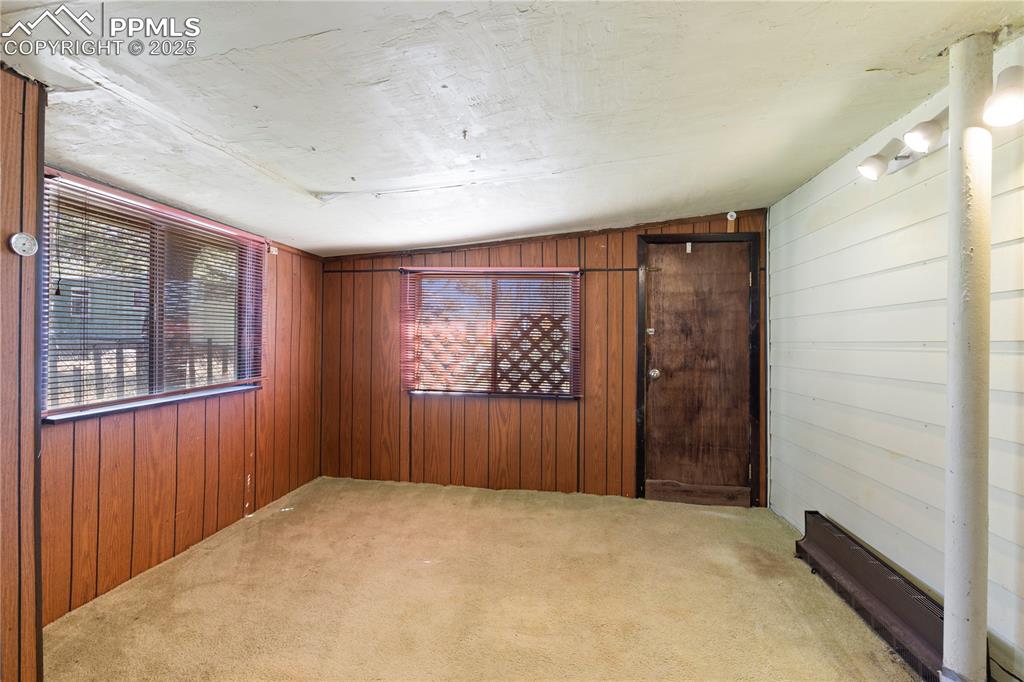 Carpeted empty room featuring wooden walls and vaulted ceiling