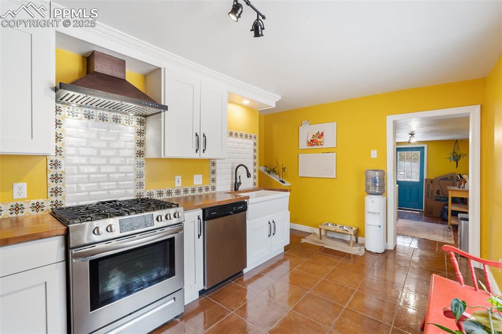 Kitchen featuring appliances with stainless steel finishes, backsplash, white cabinets, wall chimney exhaust hood, and dark tile patterned flooring