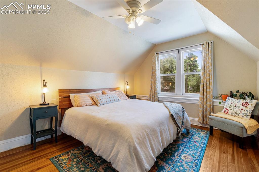 Bedroom featuring dark wood finished floors, lofted ceiling, a textured wall, and ceiling fan